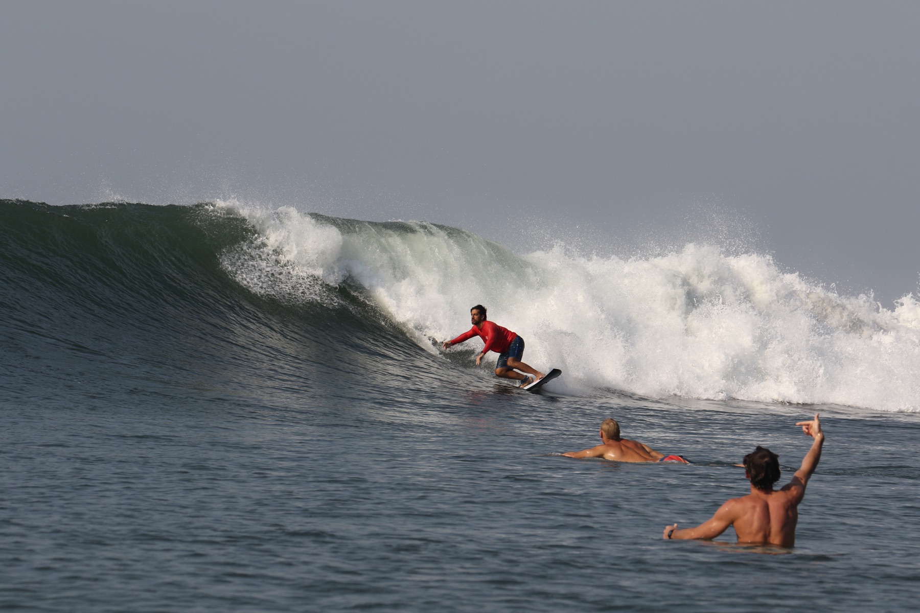 Surfer carving down the face of a steep El Salvador wave while others watch from the lineup