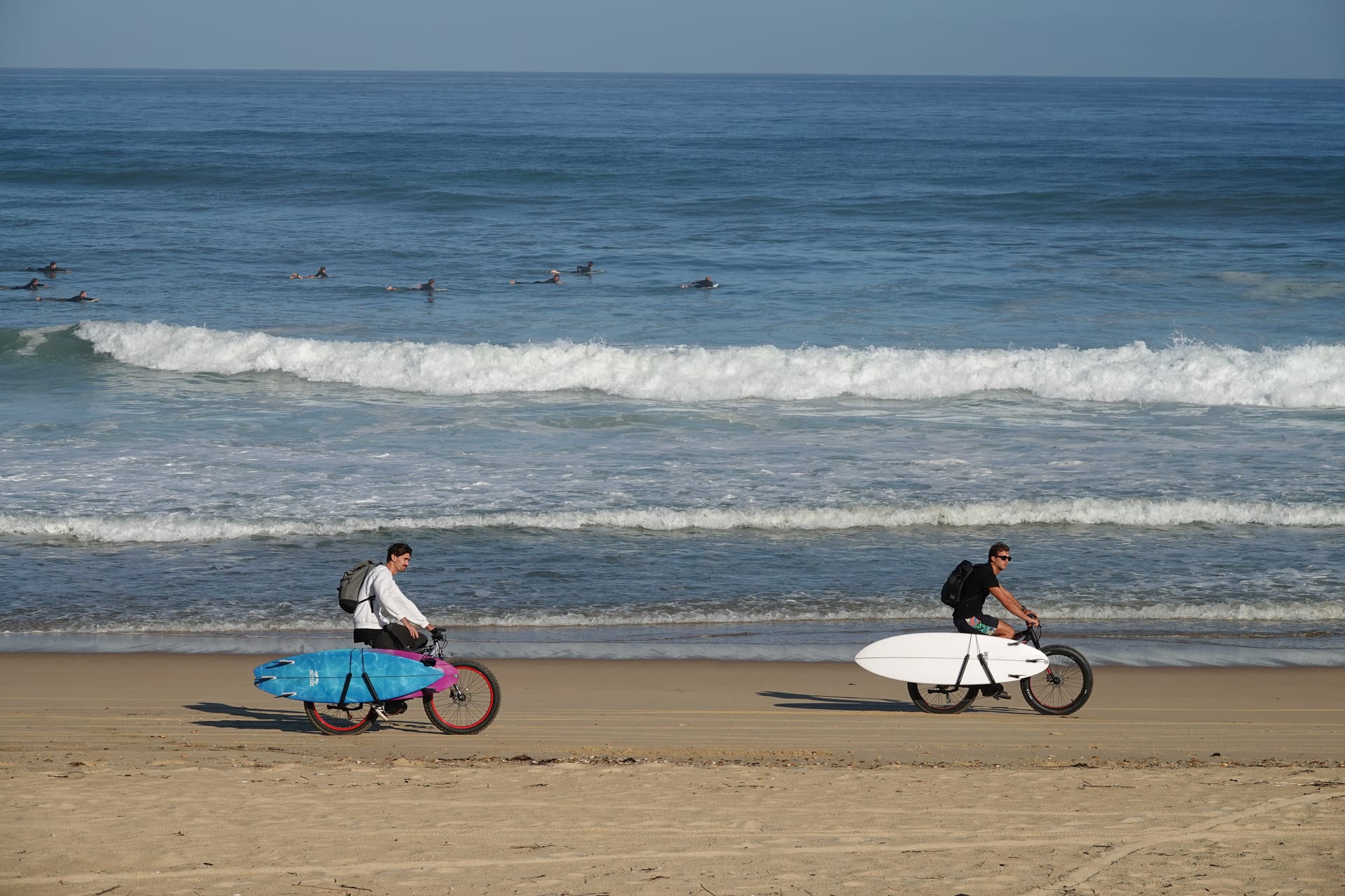 Surfers cycling along the beach with boards beside the French surf