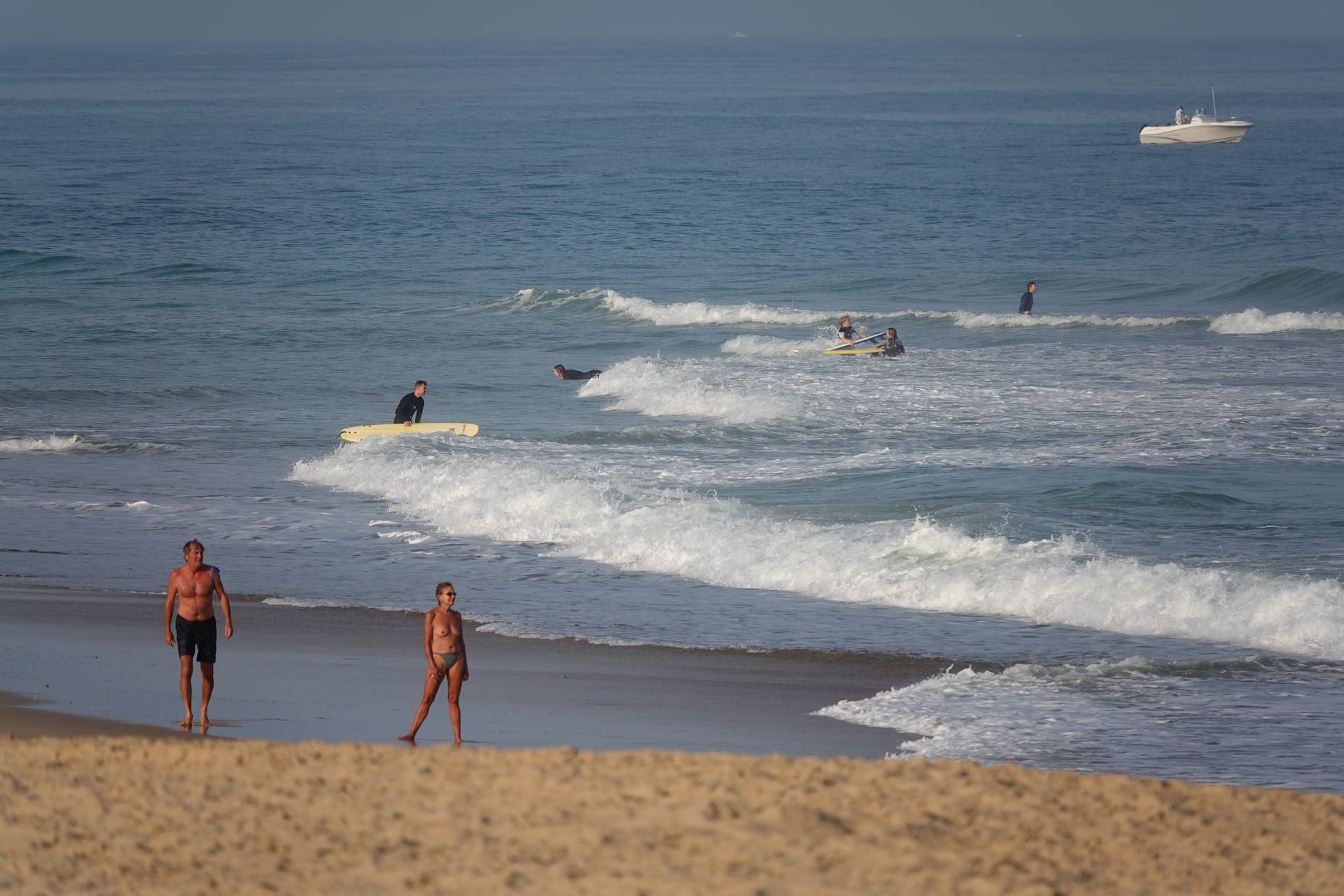 Surfers and beachgoers in mellow waves at a French beach break