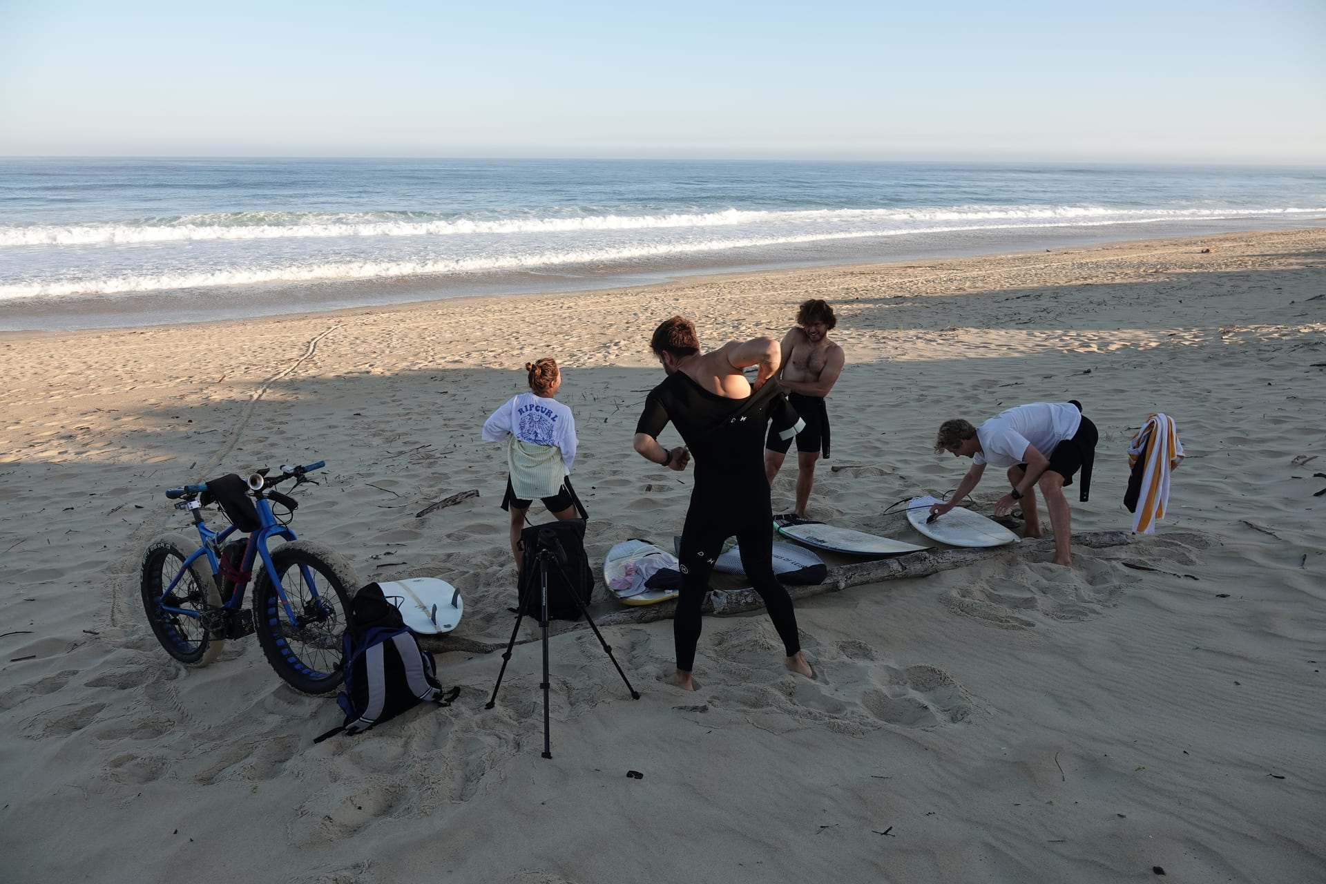 Surfers preparing boards and wetsuits on a wide sandy beach in France