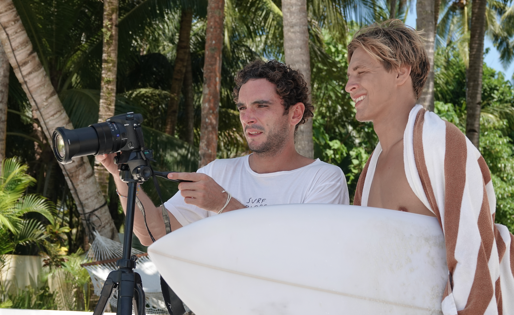 Two surfers during a SurfXplore coaching session, preparing and paddling out in tropical surf conditions.